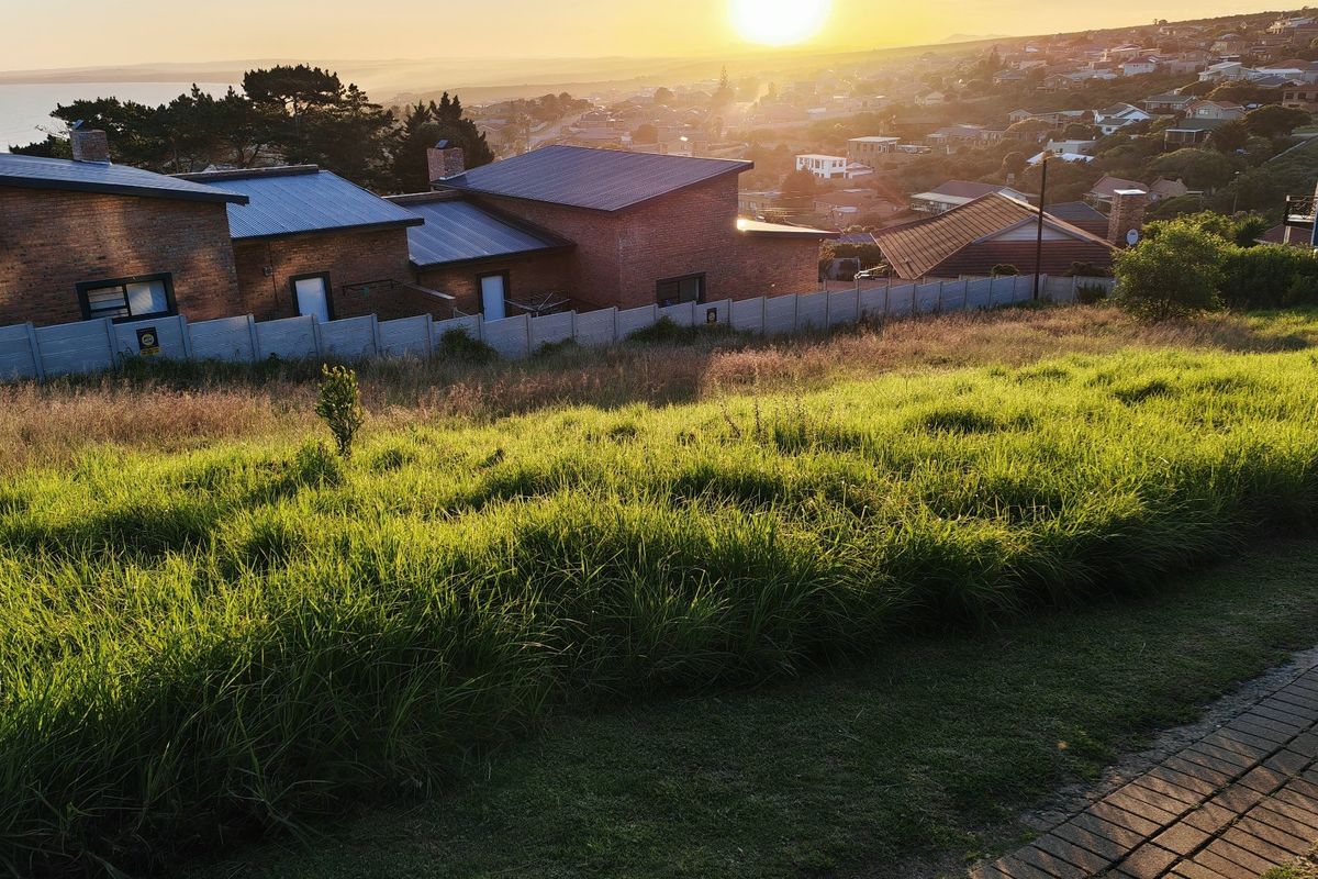 Elevated view of a vacant residential plot overlooking the surrounding neighborhood and coastline at sunset.