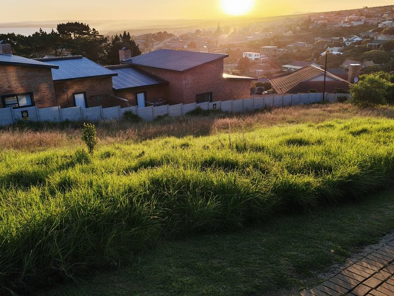 Elevated view of a vacant residential plot overlooking the surrounding neighborhood and coastline at sunset.
