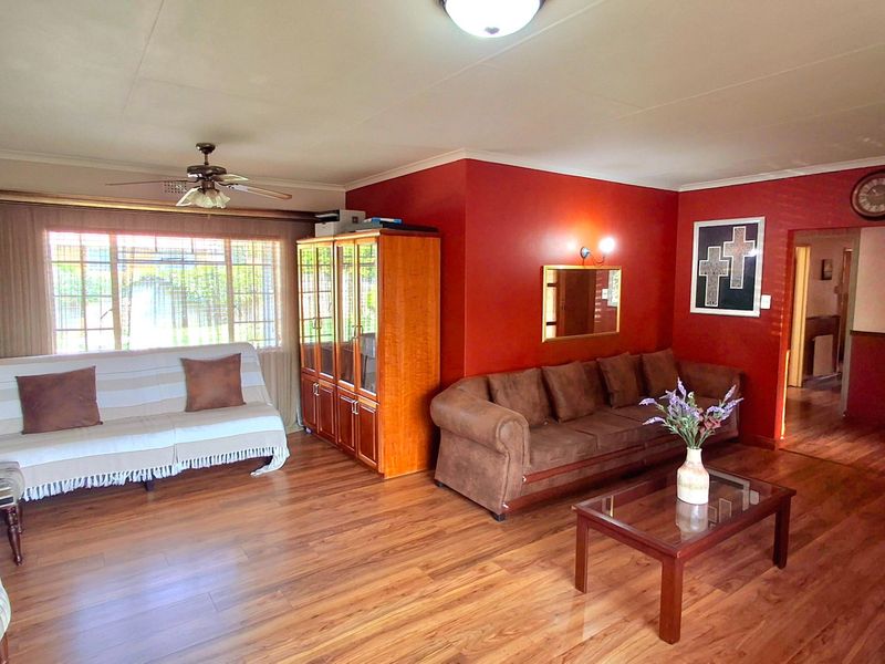 Spacious living room featuring laminate flooring, a ceiling fan, and large windows with security bars, finished with a bold red accent wall.
