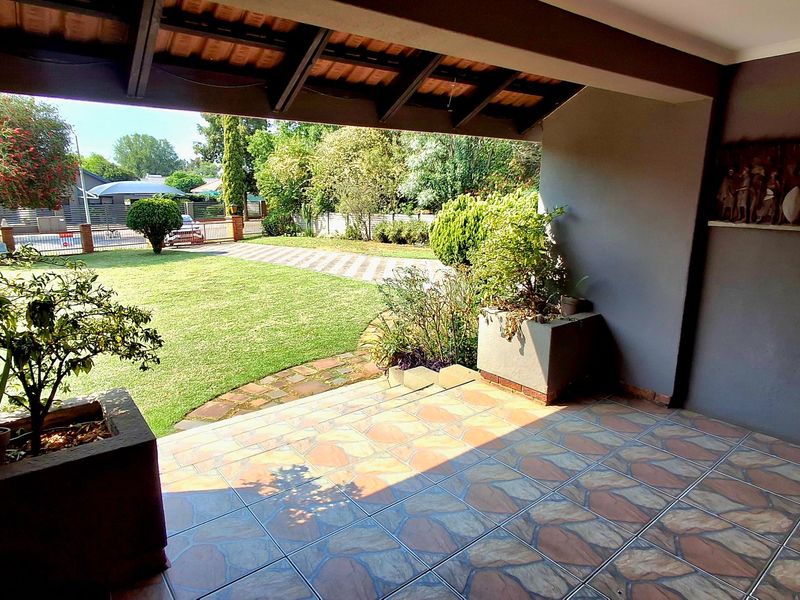 A covered patio area featuring tiled flooring, exposed timber rafters, and built-in masonry planters, overlooking a well-maintained garden.