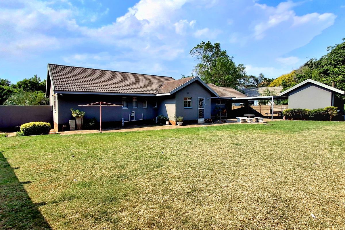 Spacious rear garden featuring a well-maintained lawn, paved patio area, and a detached garage, providing ample outdoor space for recreation.