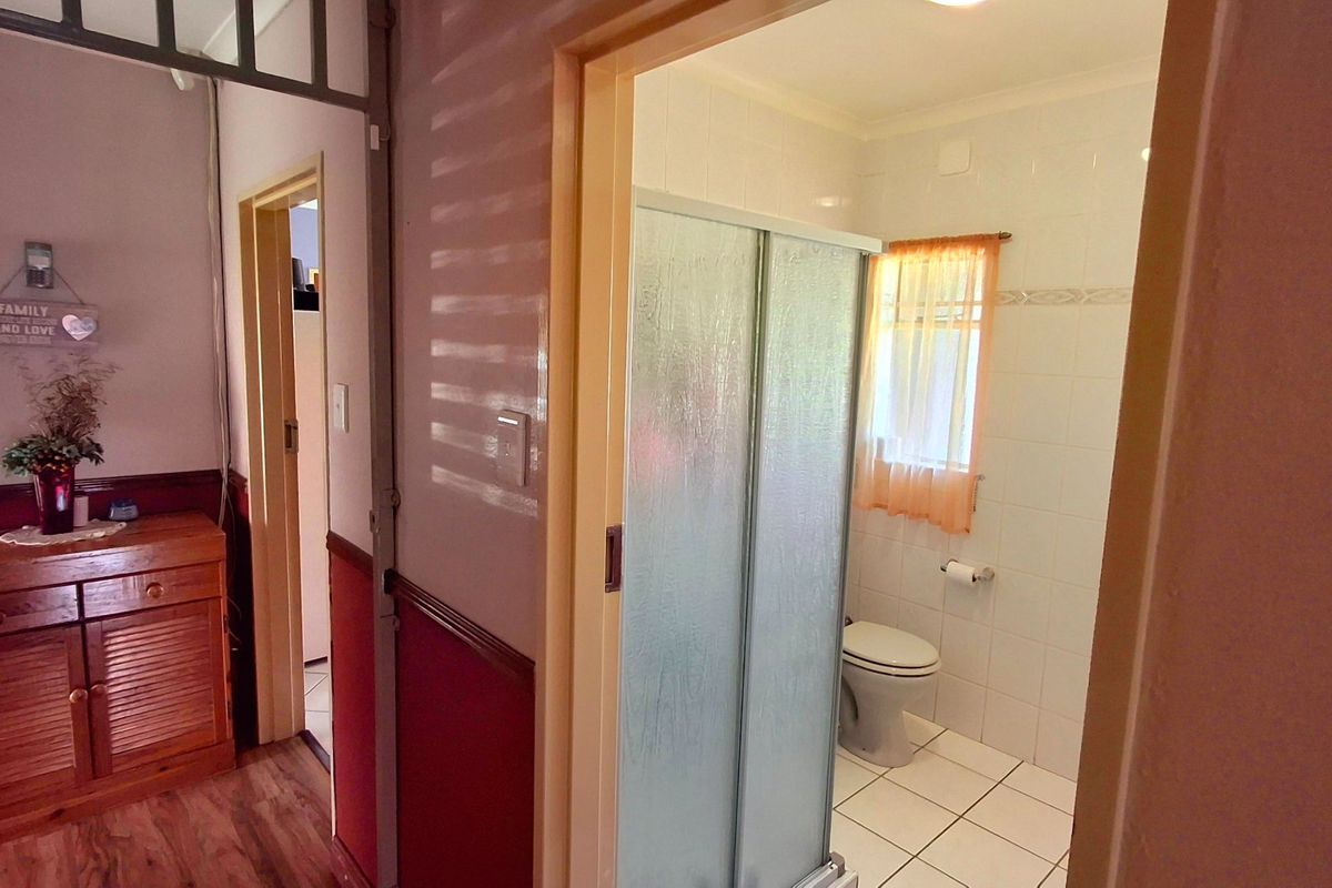 A functional bathroom featuring a shower enclosure and tiled finishes, viewed from an adjacent hallway area.