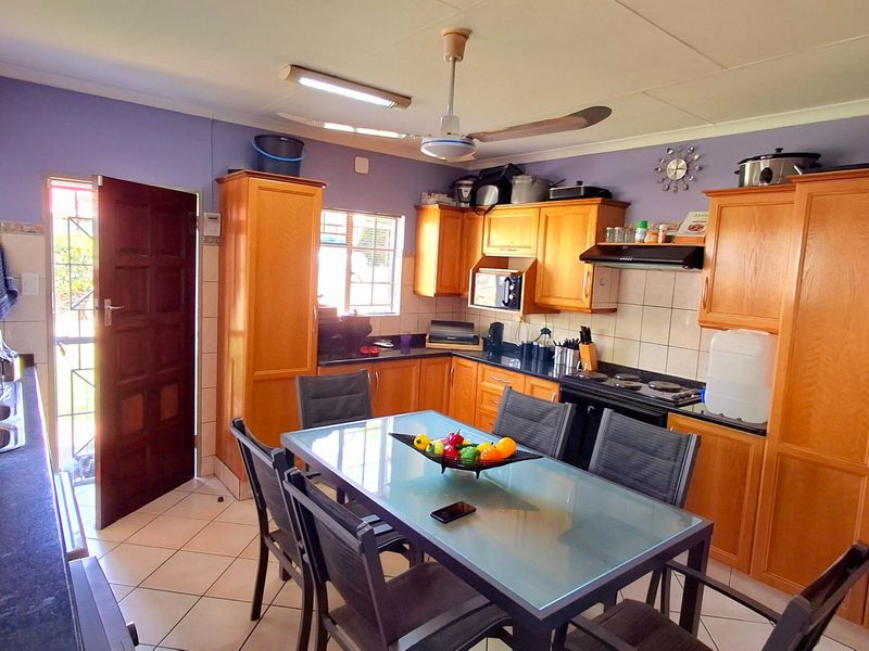 Open-plan kitchen and dining area featuring wooden cabinetry, built-in appliances, tiled flooring, and direct access to the exterior.