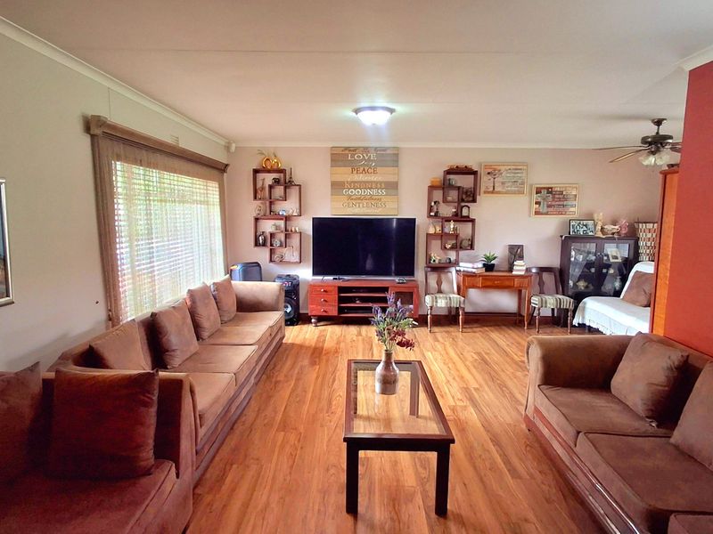 Spacious living room featuring warm-toned laminate flooring, a ceiling fan, and neutral wall finishes, providing a comfortable and inviting family space.