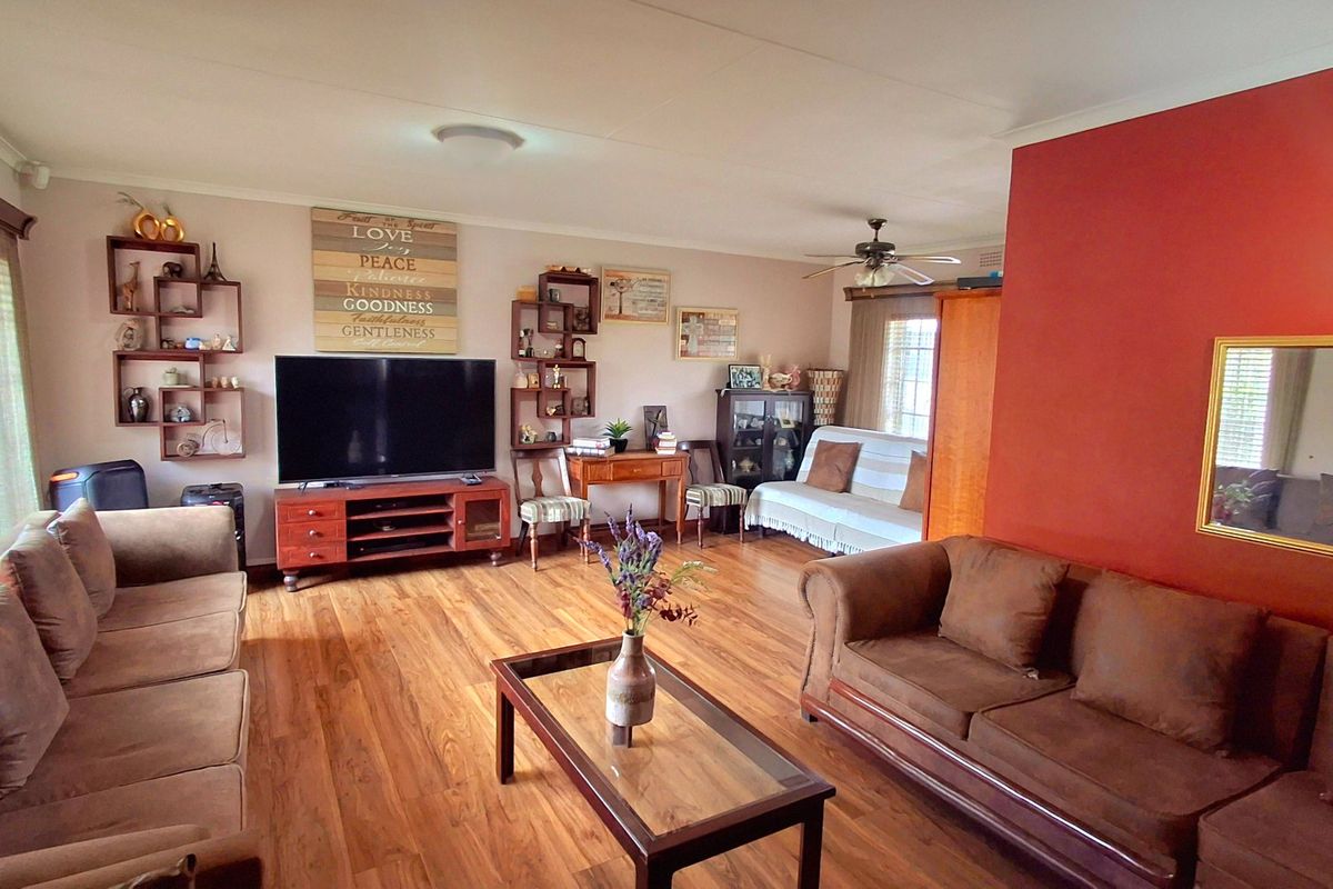 Spacious living room featuring laminate flooring, a ceiling fan, and a prominent accent wall, offering a comfortable and functional layout.