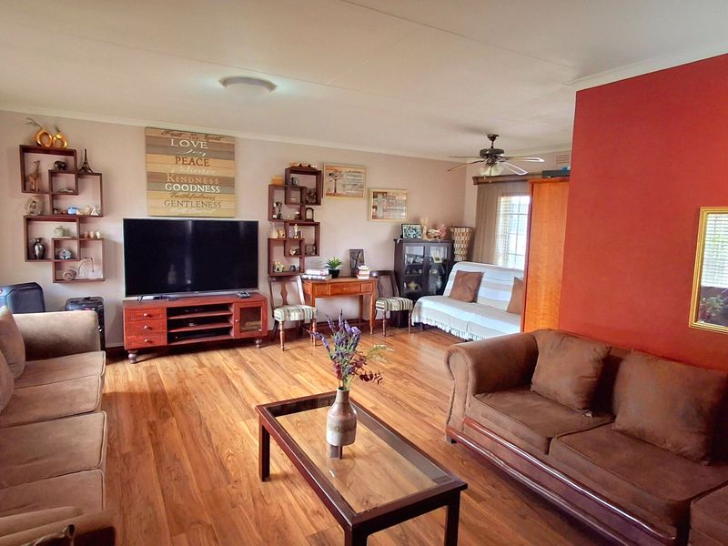 Spacious living room featuring laminate flooring, a ceiling fan, and a prominent accent wall, offering a comfortable and functional layout.