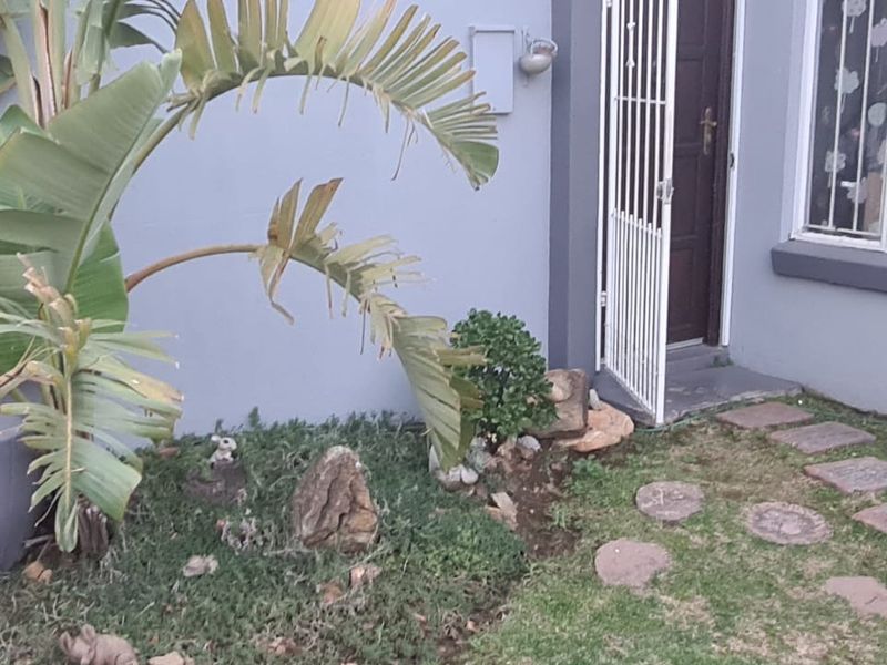 Front entrance of the townhouse featuring a security gate, security bars on the window, and a paved garden walkway.