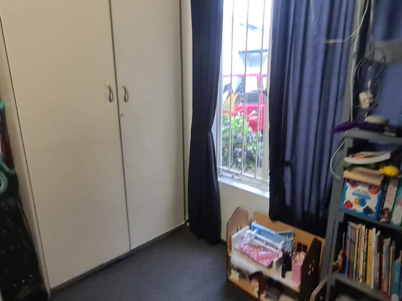 A bedroom featuring built-in cupboards and a window fitted with security bars.