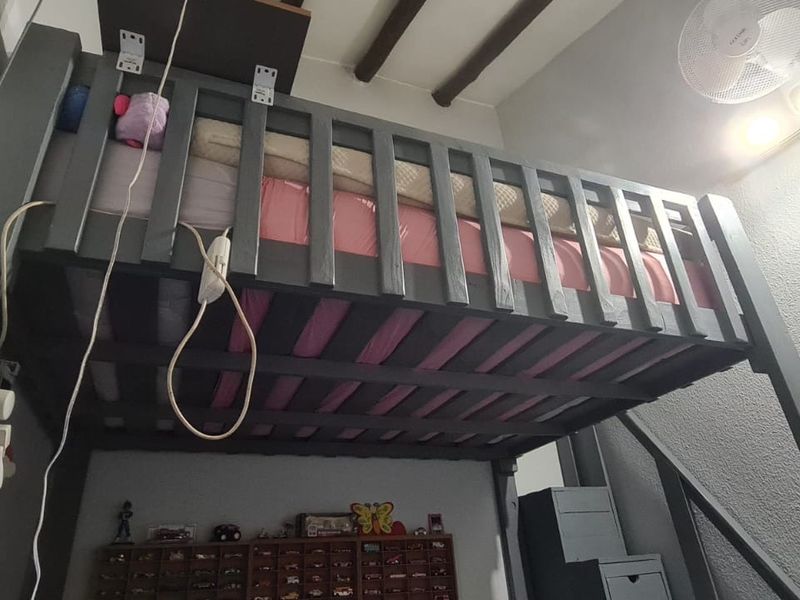 A bedroom featuring a custom loft bed structure, exposed ceiling beams, and wall-mounted lighting, requiring minor cosmetic repairs to wall finishes and electrical tidying.