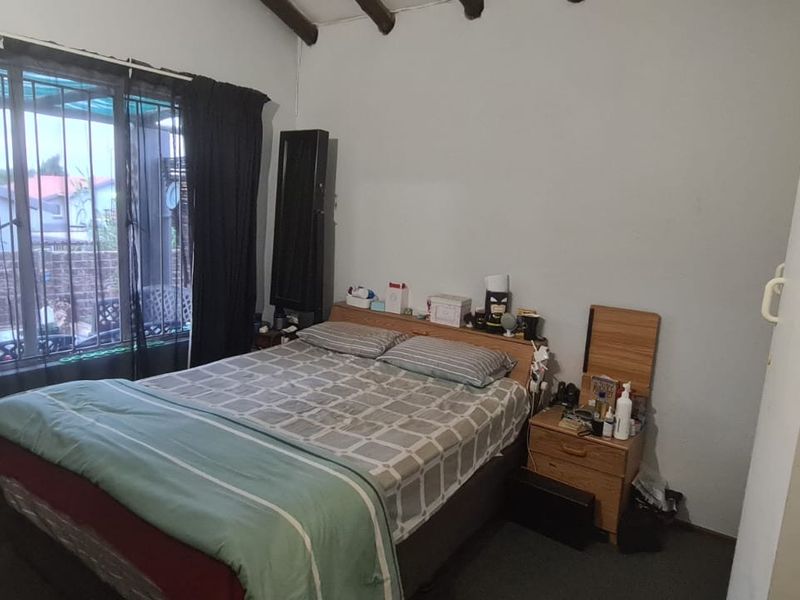 A bedroom featuring exposed timber ceiling beams and a window with security bars, offering a functional space with potential for cosmetic updates.