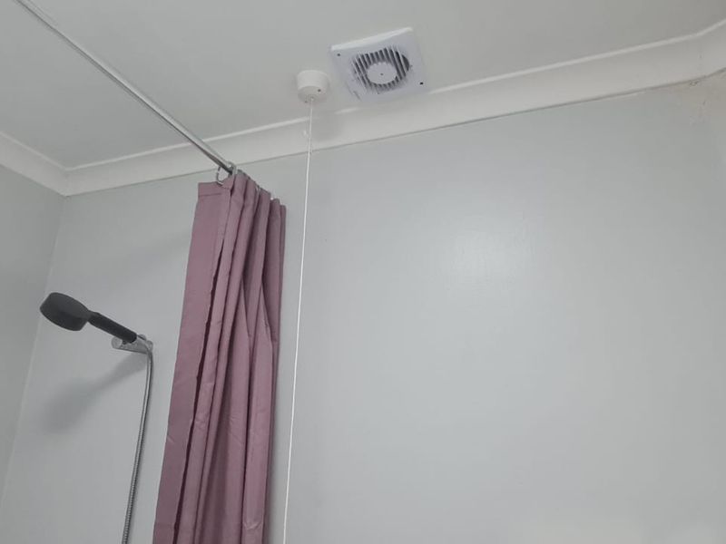 A bathroom shower area featuring a wall-mounted shower head, extractor fan, and coving, showing signs of water staining on the wall.