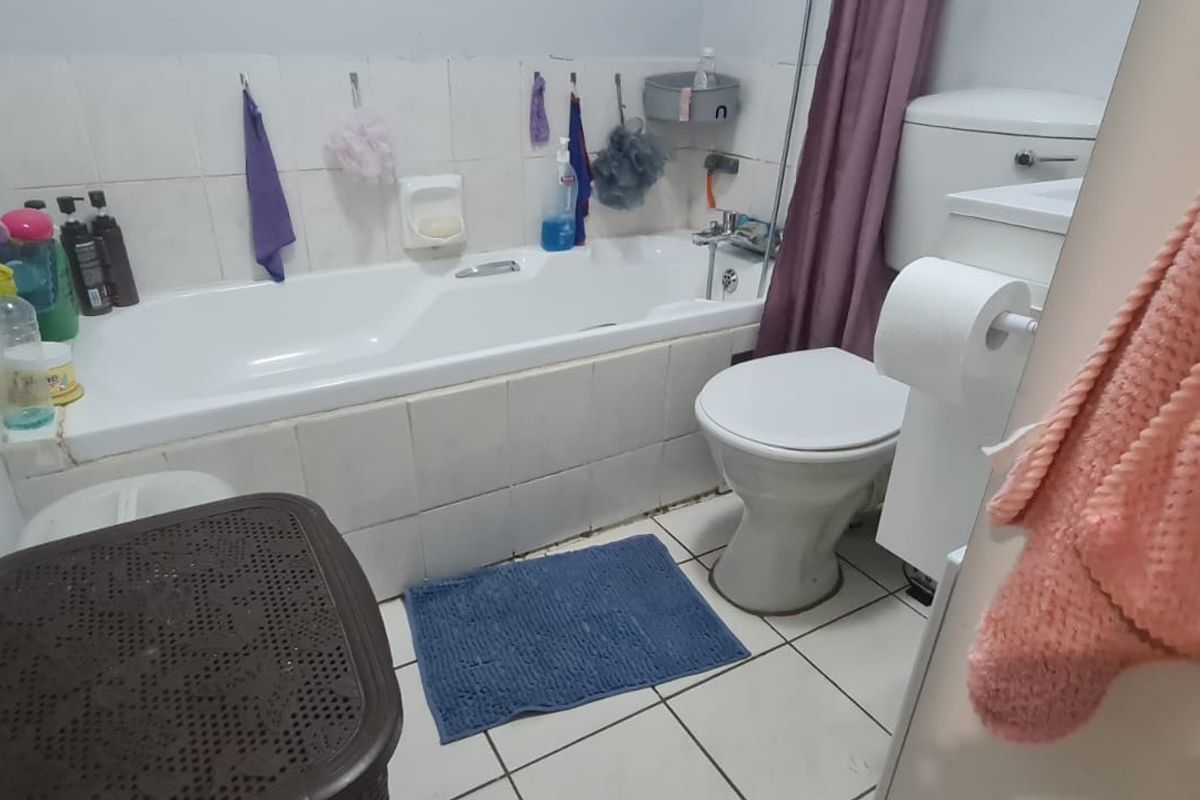 A functional bathroom featuring a standard bathtub, toilet, and tiled finishes, currently showing signs of wear and dated aesthetic.