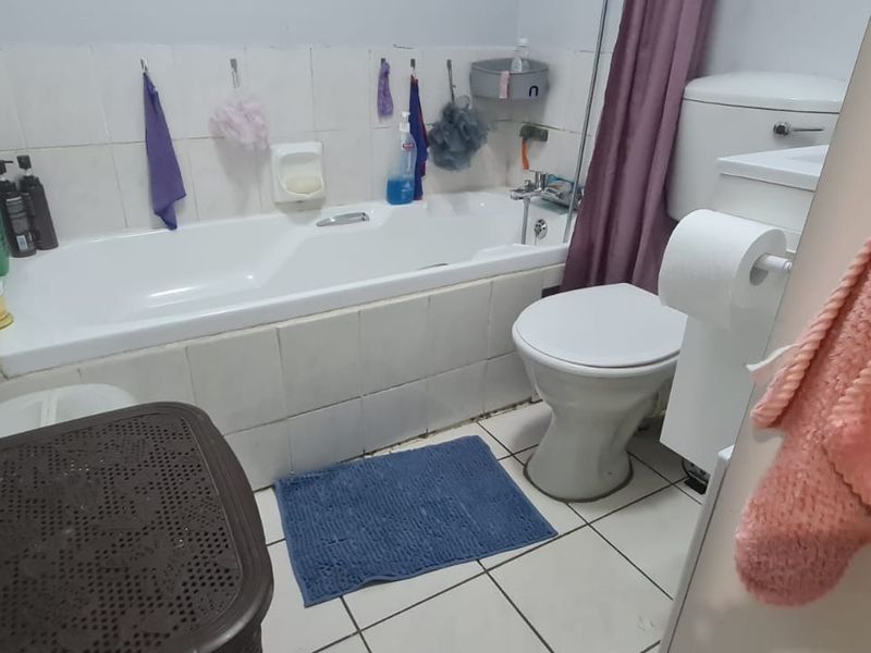 A functional bathroom featuring a standard bathtub, toilet, and tiled finishes, currently showing signs of wear and dated aesthetic.
