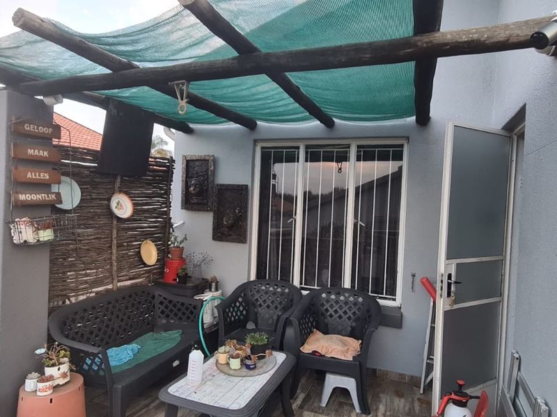 Covered patio area featuring a timber pergola with shade cloth, tiled flooring, and security features on the window and door.