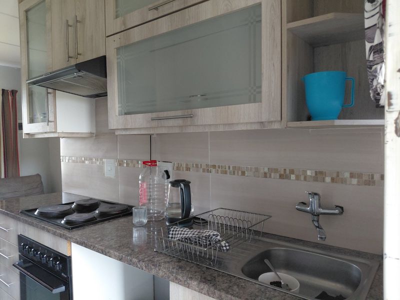 A functional kitchen featuring laminate cabinetry, a tiled backsplash, an electric hob with extractor fan, and a stainless steel sink.