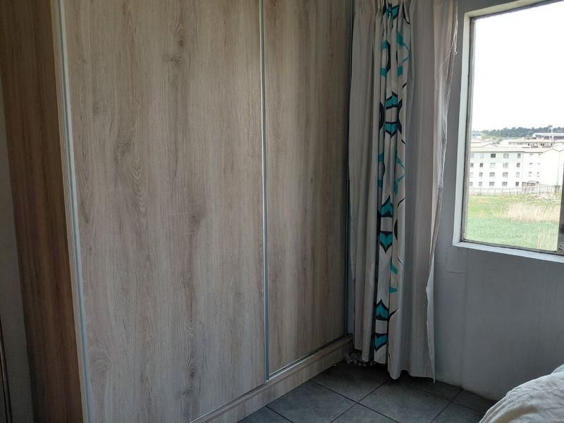 A bedroom featuring a modern wood-finish built-in wardrobe and tiled flooring, with a window providing natural light and exterior views.