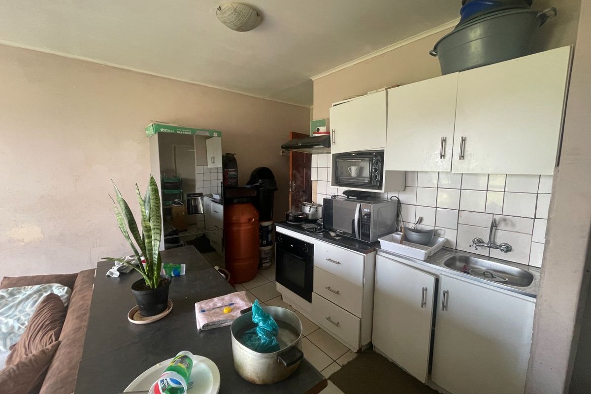 A compact kitchen featuring white built-in cabinetry, a tiled backsplash, and integrated oven with extractor fan, requiring cosmetic updates to improve overall condition.