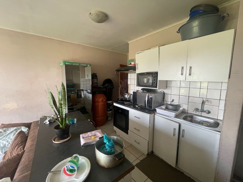 A compact kitchen featuring white built-in cabinetry, a tiled backsplash, and integrated oven with extractor fan, requiring cosmetic updates to improve overall condition.