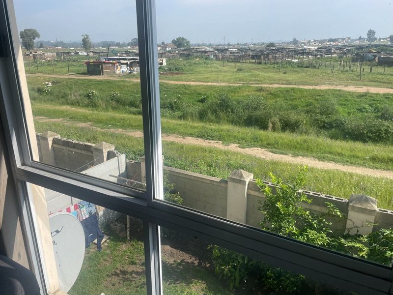 An elevated view from an apartment window looking out over a grassy field and surrounding residential area.