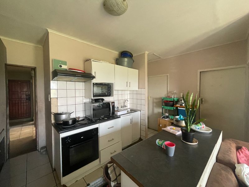 A compact kitchen featuring built-in cabinetry, an electric oven with hob, extractor fan, and a tiled backsplash, offering a functional layout for daily use.