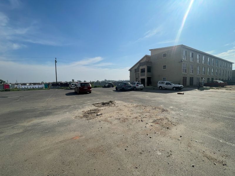 Exterior view of a multi-story apartment complex featuring a large asphalt parking area with visible surface damage and potholes.