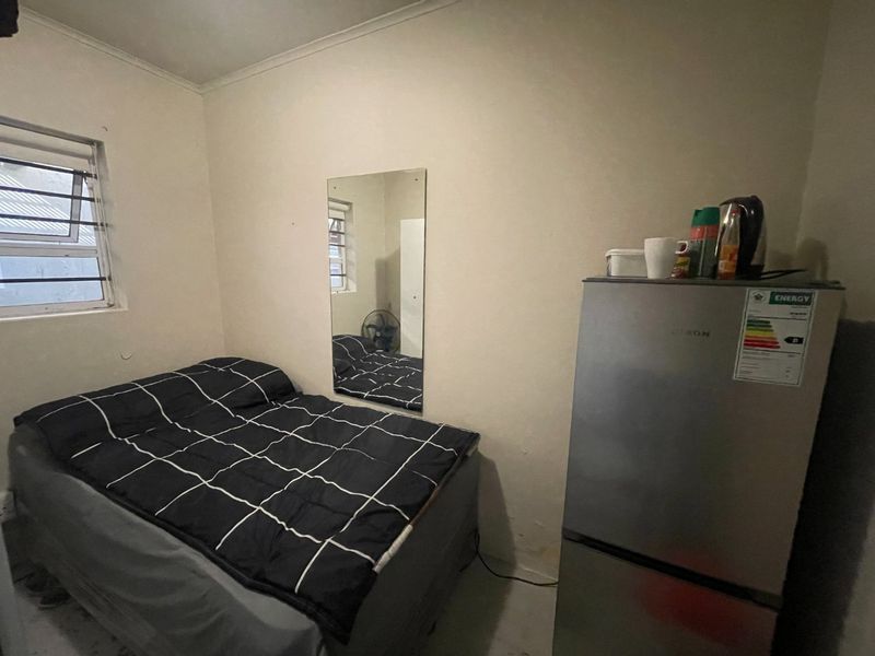 A compact bedroom featuring a louvered window and a wall-mounted mirror, requiring cosmetic updates to improve the overall finish and appeal.