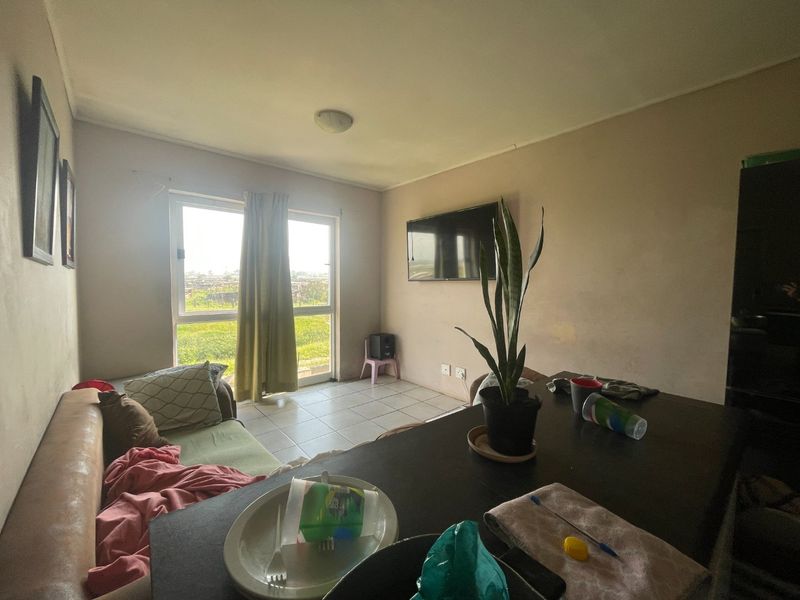 A living room area featuring tiled flooring and a sliding glass door leading to an outdoor view, with a wall-mounted television.