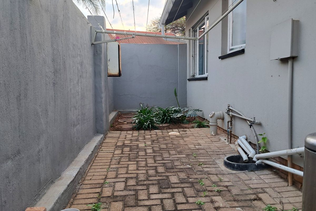 A paved rear courtyard area featuring boundary walls, external plumbing connections, and a wall-mounted washing line.
