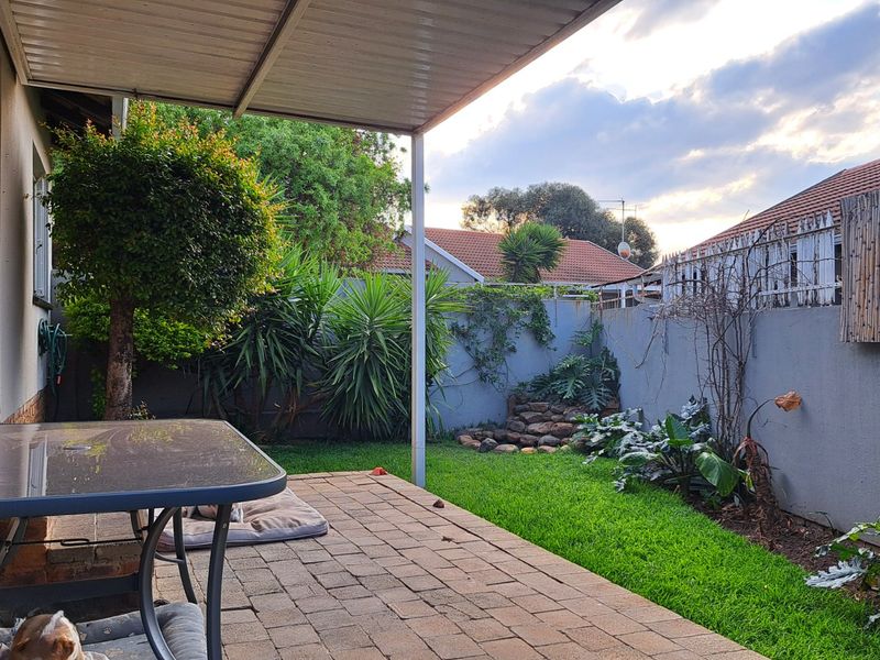 A covered patio area featuring paved flooring, overlooking a private garden with established landscaping and boundary walls.