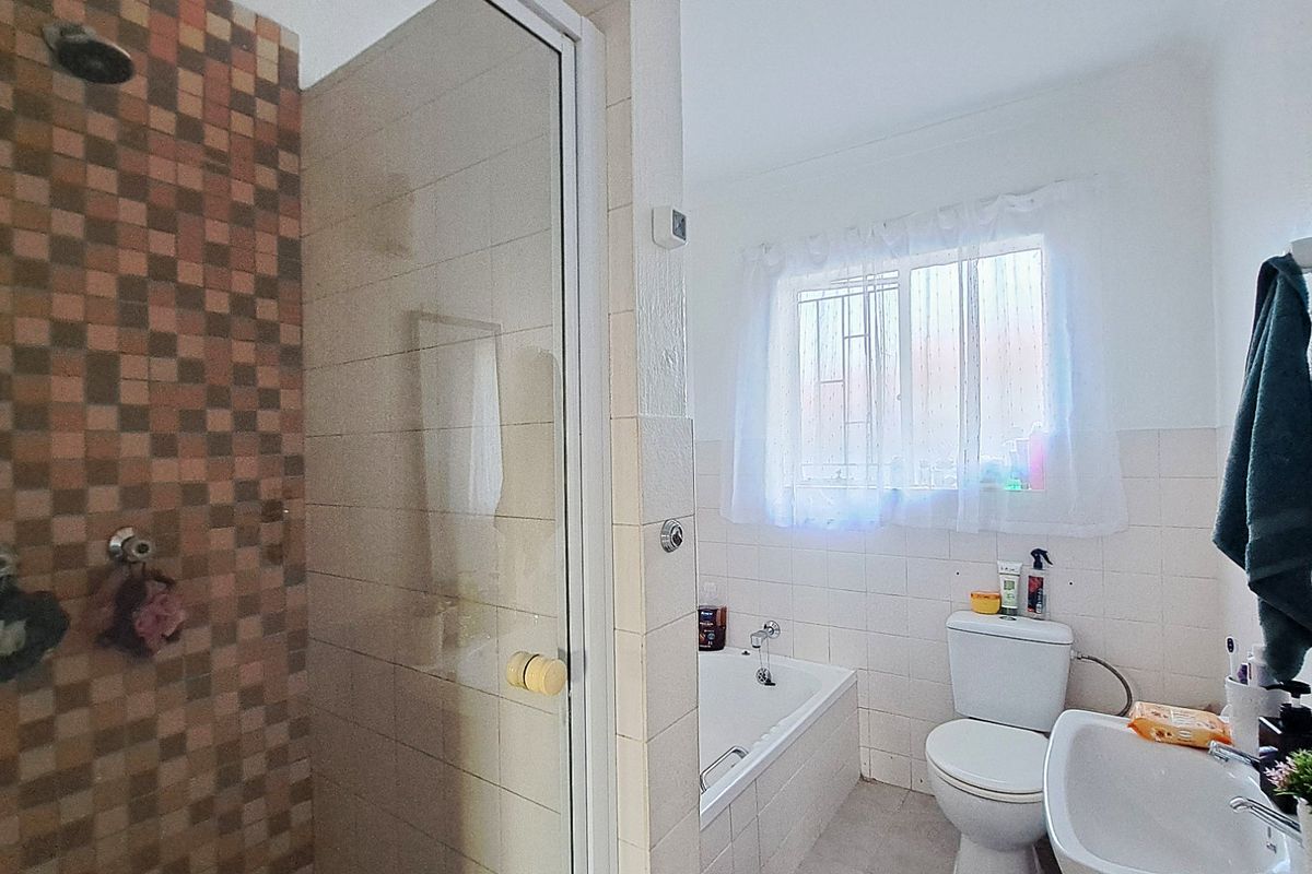 A functional bathroom featuring a separate shower enclosure, built-in bathtub, toilet, and washbasin with tiled finishes and a window with security bars.