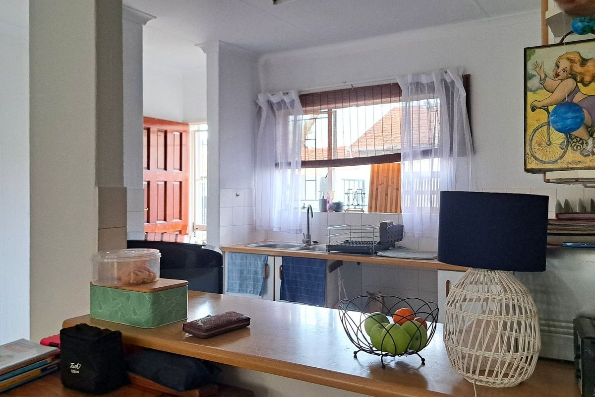 A functional kitchen area featuring a wooden breakfast bar, tiled backsplash, and a sink overlooking the exterior through a window with security bars.