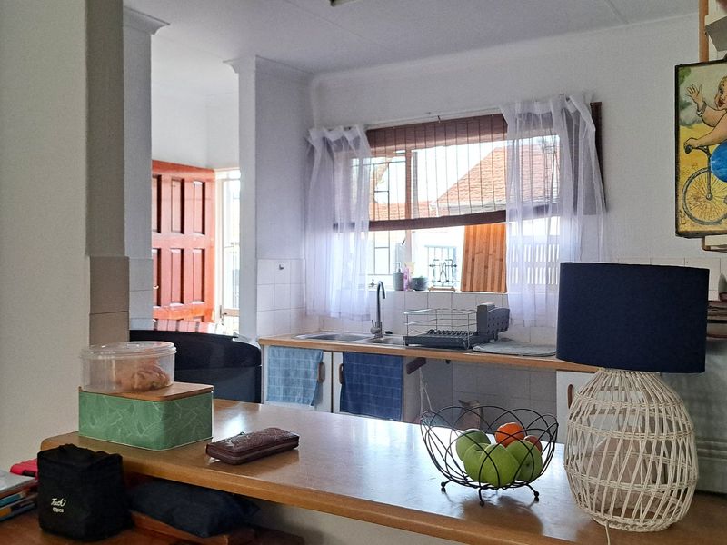 A functional kitchen area featuring a wooden breakfast bar, tiled backsplash, and a sink overlooking the exterior through a window with security bars.