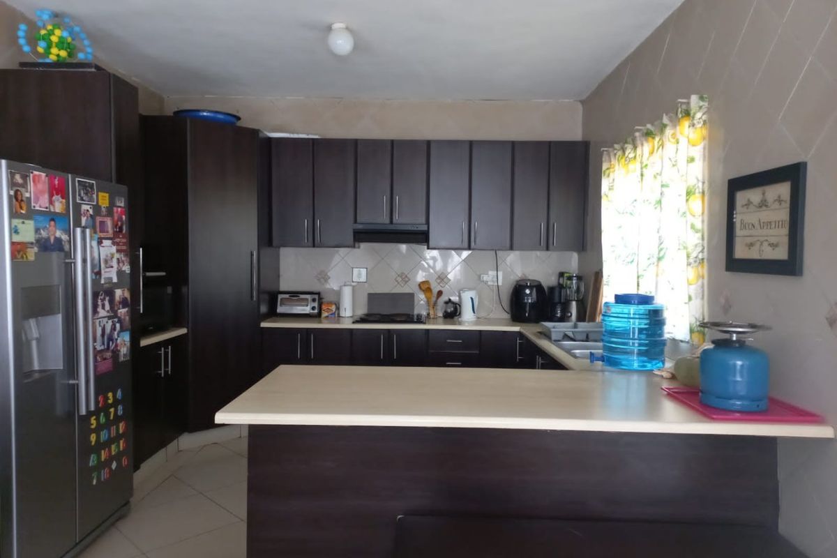 A functional kitchen featuring dark wood cabinetry, laminate countertops, a tiled backsplash, and a breakfast bar area with tiled flooring.