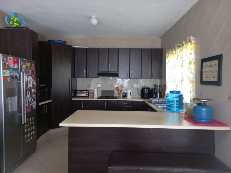 A functional kitchen featuring dark wood cabinetry, laminate countertops, a tiled backsplash, and a breakfast bar area with tiled flooring.