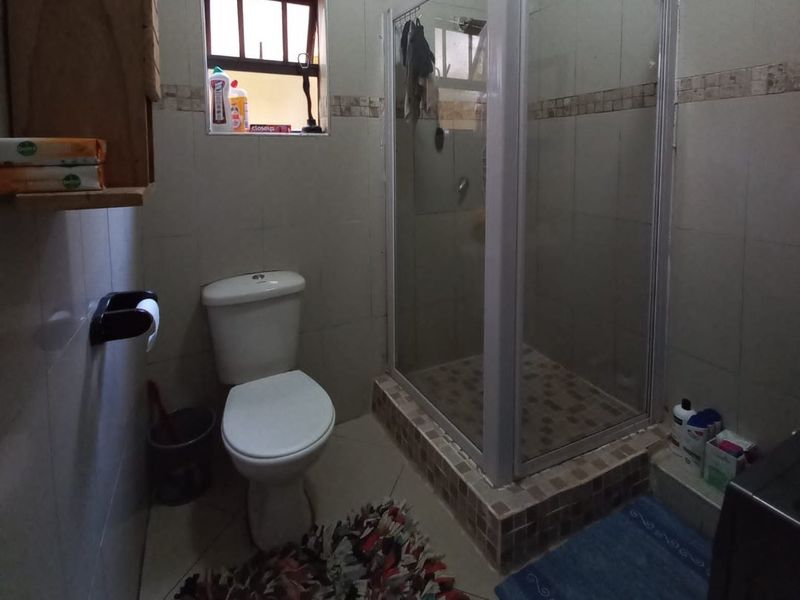 A functional bathroom featuring a tiled shower enclosure, standard toilet, and neutral wall tiling, offering a practical layout for an apartment.
