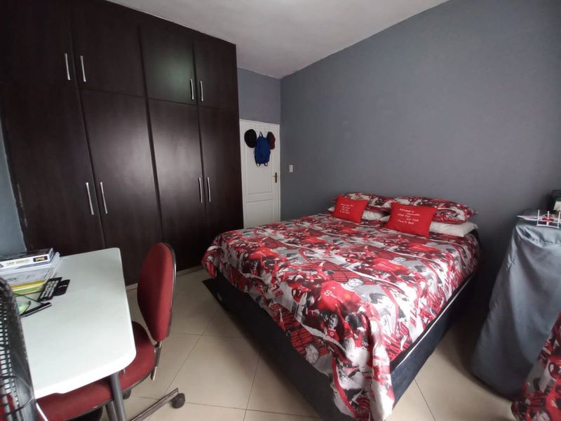 A bedroom featuring dark wood built-in cupboards and neutral floor tiles, providing a functional space with ample storage.