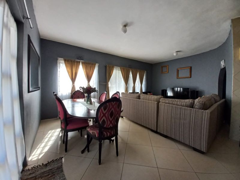 Open-plan living and dining area featuring tiled flooring and large windows with curtain rails, providing a functional and versatile space.