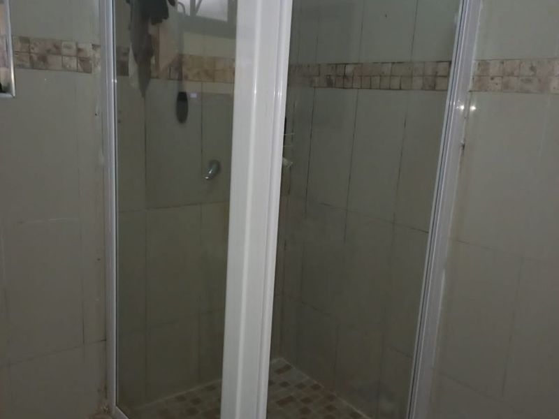 A bathroom featuring a corner shower enclosure with a raised tiled base and neutral wall tiling.