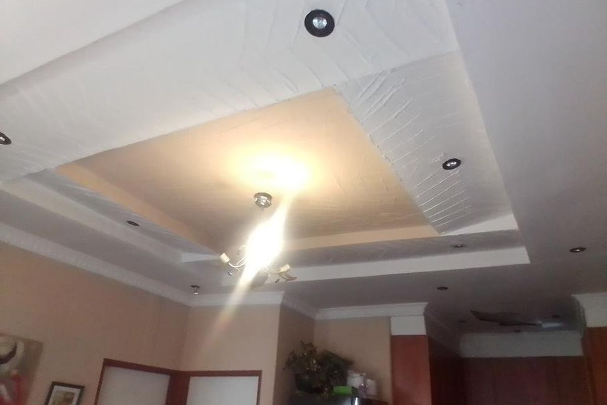 A view of a living room ceiling featuring a recessed design with integrated downlights and a central chandelier, showing signs of ceiling damage.