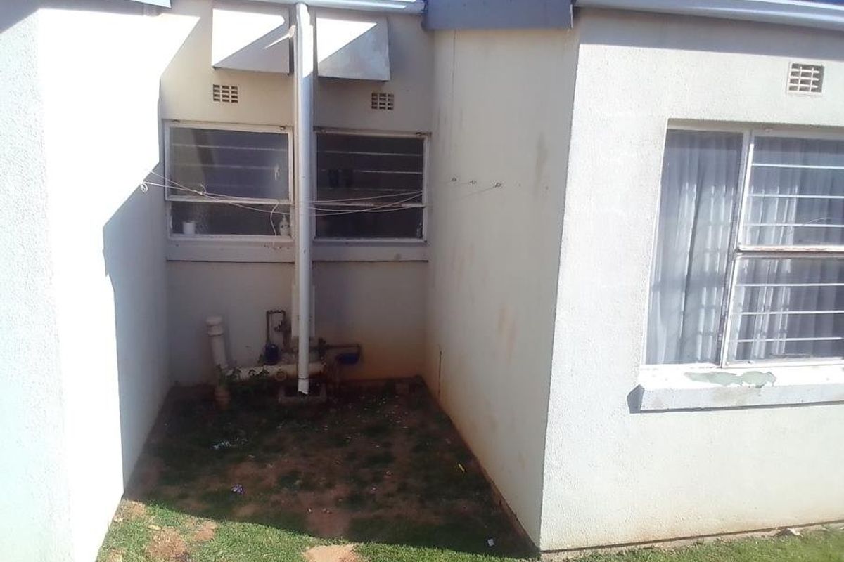 Rear exterior view of the townhouse showing exposed plumbing, security bars on windows, and visible wear on the exterior wall finishes.