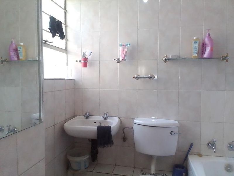 A functional bathroom featuring a wall-mounted basin, toilet, and bathtub with tiled walls and flooring, requiring some cosmetic updates.