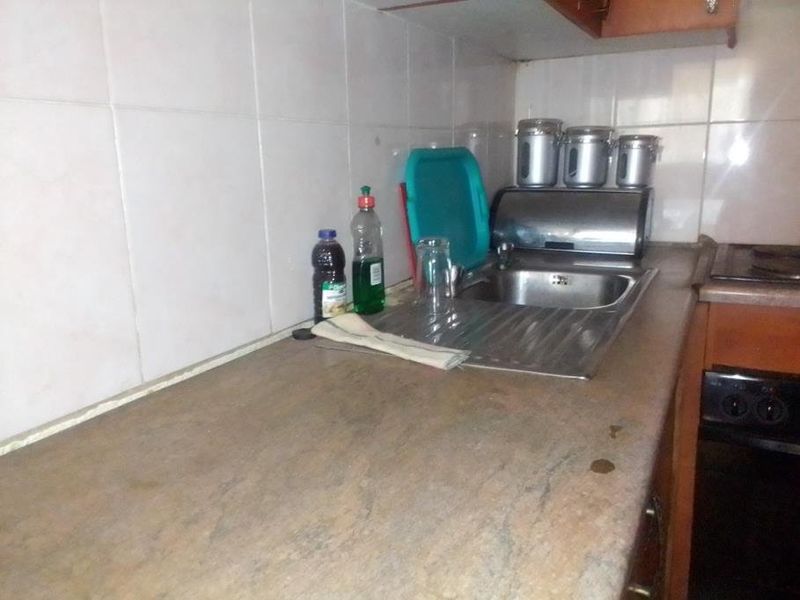 A dated kitchen area featuring a laminate countertop, stainless steel sink, and tiled splashback, requiring cosmetic updates to improve its overall appeal.