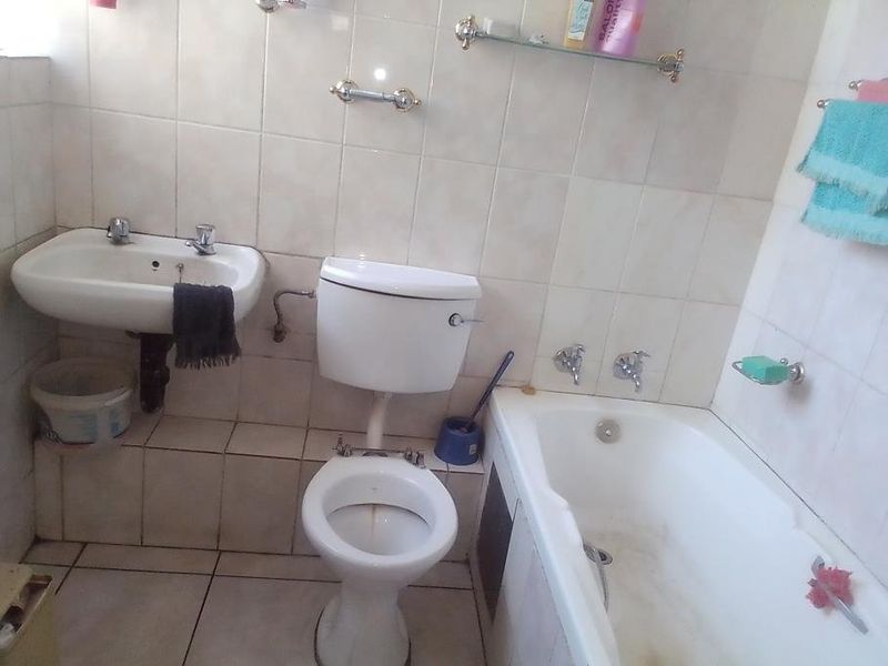 A dated bathroom featuring a wall-mounted basin, standard toilet, and bathtub with tiled walls and flooring, requiring cosmetic updates and maintenance.