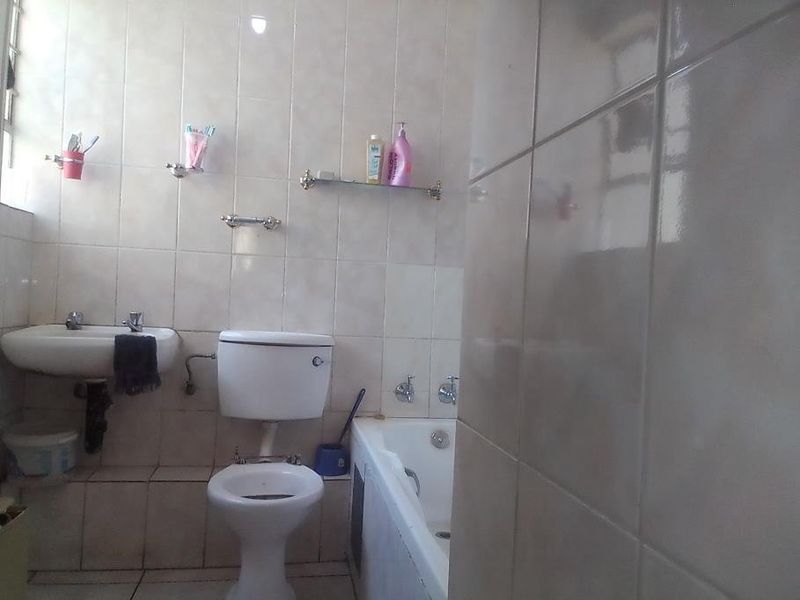 A functional bathroom featuring a wall-mounted basin, toilet, and bathtub with full-height ceramic wall tiling.