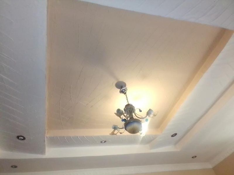 A close-up view of a recessed ceiling featuring textured plasterwork, integrated downlights, and a central pendant light fixture.