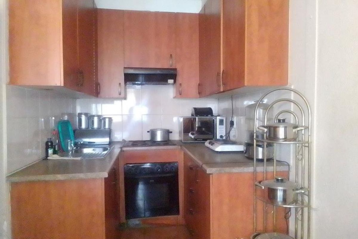 A compact galley-style kitchen featuring wooden cabinetry, built-in oven, hob, extractor fan, and tiled splashbacks, offering functional storage and preparation space.