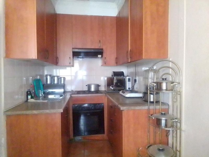 A compact galley-style kitchen featuring wooden cabinetry, built-in oven, hob, extractor fan, and tiled splashbacks, offering functional storage and preparation space.