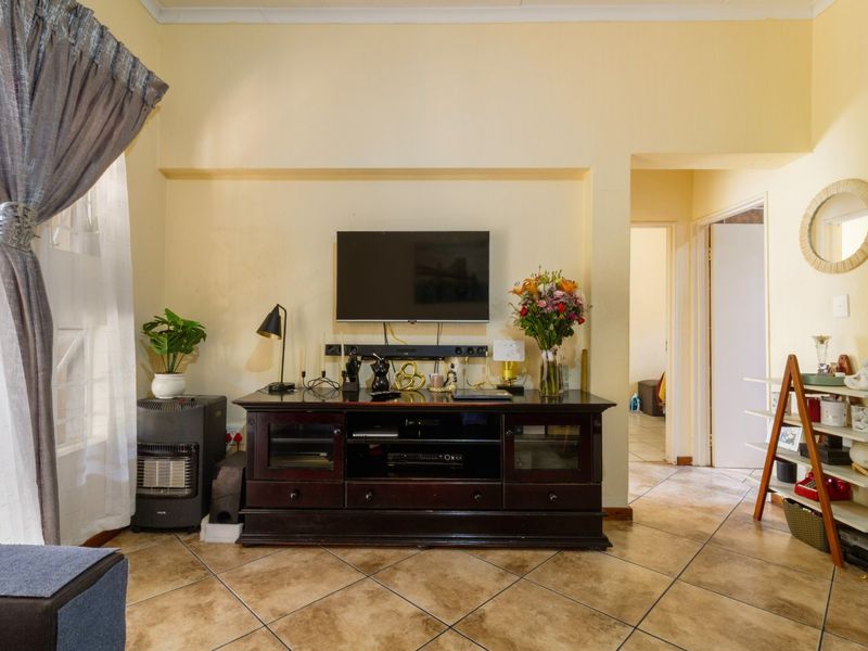 A living room featuring tiled flooring and neutral wall finishes, providing a functional space with access to adjacent rooms.