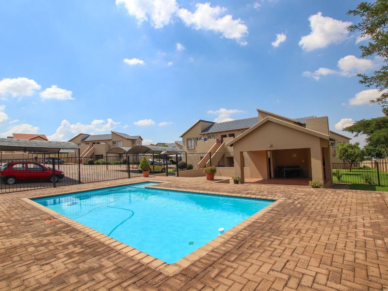 A well-maintained communal pool area featuring a paved deck, covered patio space, and surrounding metal fencing within an apartment complex.
