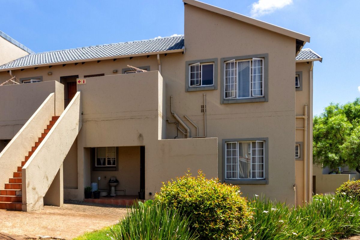 Rear view of a multi-story apartment building featuring an external staircase, tiled roof, and paved ground area with established garden landscaping.